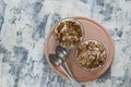 Dessert granola, Greek yogurt, kiwi and banana in two glass cups with spoons on a wooden round board, gray concrete, flat lay.