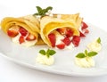 A dessert plate with pancakes, strawberry, whipped cream and mint