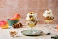 Dessert, portioned apple trifle with oat crumble, spiced cake, custard and whipped cream in a glass goblet on a light concrete
