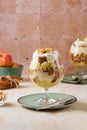 Dessert, portioned apple trifle with oat crumble, spiced cake, custard and whipped cream in a glass goblet on a light concrete