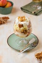 Dessert, portioned apple trifle with oat crumble, spiced cake, custard and whipped cream in a glass goblet on a light concrete