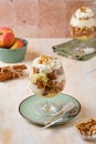 Dessert, portioned apple trifle with oat crumble, spiced cake, custard and whipped cream in a glass goblet on a light concrete