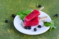 Dessert, portioned homemade ice cream or popsicles made from red currants and blackberries on a white plate against a green