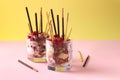 Dessert in two glasses with chocolate granola, banana and raspberry, decorated with sticks Pocky on yellow and pink background Royalty Free Stock Photo