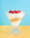 A dessert from whipped cream, greek yogurt, ice cream and biscuits with maraschino cherry in a glass.