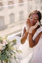 Destination fine-art wedding in Florence, Italy. African-American bride sits at the table, touches her face with gloves