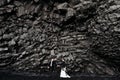 Destination Iceland wedding. Wedding couple under a rock of basalt stones. Bride and groom on the black beach of Vik. Royalty Free Stock Photo