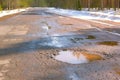 Destroyed broken asphalt road with holes, melting snow and puddles early spring.