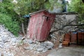 Destroyed cracked traditional outdoor wooden toilet leaning to one side with broken dilapidated boards surrounded with rocks and