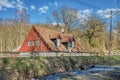 Detached rural red countryside house by a river with a short waterfall or farmhouse by a countryside road in the bare woods Royalty Free Stock Photo