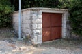 Detached small garage with rusted metal doors and stone walls next to gravel road surrounded with dense trees and vegetation