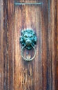 Detail of an ancient wooden door aged by time with a metal lion head shaped door knocker with a ring in the mouth
