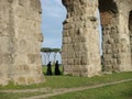 Roman aqueduct wit two walking priests to Rome in Italy. Royalty Free Stock Photo