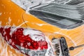 Detail on back of yellow car being washed at carwash, brush leaving strokes in white foam and shampoo.