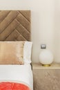 Detail of a bedroom decorated with a marble cube, a round lamp and a headboard upholstered