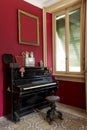 Detail of black piano with stool and shuttered window. There is a large frame hanging on the wall Royalty Free Stock Photo