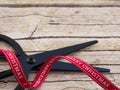 Detail of black scissor and red ribbon on wooden background