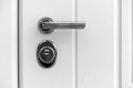 Detail of a closed door with a lock handle and a white background. Metal handle and lock on the front door