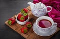 Detail of a cup of strawberry tea accompanied by porcelain teapot and strawberries loose on a rustic wooden board with a crumpled