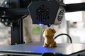 Detail of a 3D printer printing a model with a gold biodegradable PLA filament, ecofil, blue light