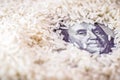 Detail of a 100 dollar banknote on white rice, concept of agribusiness and export or import of rice Royalty Free Stock Photo