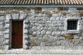 Detail of the facade of an ancient building with a stone and brick wall with a barred window and a wooden door. Royalty Free Stock Photo