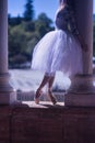 Detail of feet in classical ballet slippers of a woman in a white tutu illuminated by a ray of sunlight between two columns Royalty Free Stock Photo