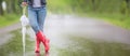 Detail of female legs in rain boots and a closed umbrella standing on the road on a rainy day Royalty Free Stock Photo