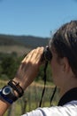 Detail of a girl holding with both hands a pair of binoculars in her eyes to see and observe the mountain landscape on a sunny day