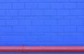 Detail of grungy blue wall with horizontal red pipe. Background in strong contrasting colors.