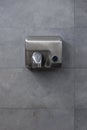 Detail of a hand dryer hanging on a gray tile wall. Front view