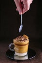 Detail of a hand holding a teaspoon ready to have the dalgona coffee cream dessert. On dark background Royalty Free Stock Photo