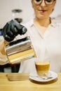 Detail of the hands of a waiter, behind the bar of a restaurant preparing a coffee with milk. Inside