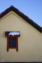 Detail of a house with a small window with a dark red frame and a snow covered small roof. Royalty Free Stock Photo