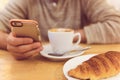 Detail image of unrecognisable man drinking coffee and holding smart phone while having breakfast in restaurant.