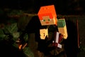 Detail of LEGO Minecraft Alex action figure creeping out of hole under real wooden bridge, equipped with pickaxe.