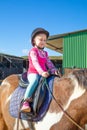 Detail of cute little girl riding a horse next to the stable Royalty Free Stock Photo