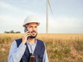 Detail of a male wind engineer with a safety helmet talking on the phone in a field of windmills. Renewable energy