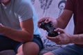Detail of man`s hand holding a video console controller while playing with a friend