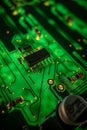 Detail of a microprocessor, resistors and capacitors soldered to a green glowing PCB