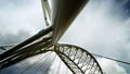 Detail of modern white metal bridge with steel support wires seen from below with blue sky and clouds