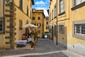 Detail of narrow street in old historic alley in the medieval City of Cortona with people on restaurant outdoor tables