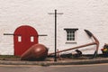 Detail of an old barn red door with black metal hinges against a white wall and a huge anchor outside Royalty Free Stock Photo