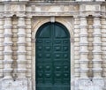 Detail of an old urban building stone facade with tall green wood door and decorative columns