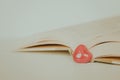 Detail of one very small red heart among open vintage book on white surface, copy space. Love Pieces in Literature Royalty Free Stock Photo