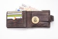 Detail of an open leather wallet with a big golden Bitcoin, fiat notes and credit cards and blue lit keyboard in