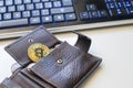 Detail of an open leather wallet with a big golden Bitcoin, fiat notes and credit cards and blue lit keyboard in