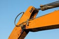 Detail on orange arm of excavator machine, hydraulic piston mechanism and joint dirty from black oil visible. Afternoon blue sky