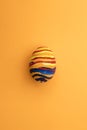 Detail of painted yellow Easter egg with red and blue stripes in orange background Royalty Free Stock Photo