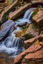 Detail of pair of small cascading waterfalls pouring over mossy boulders in creek